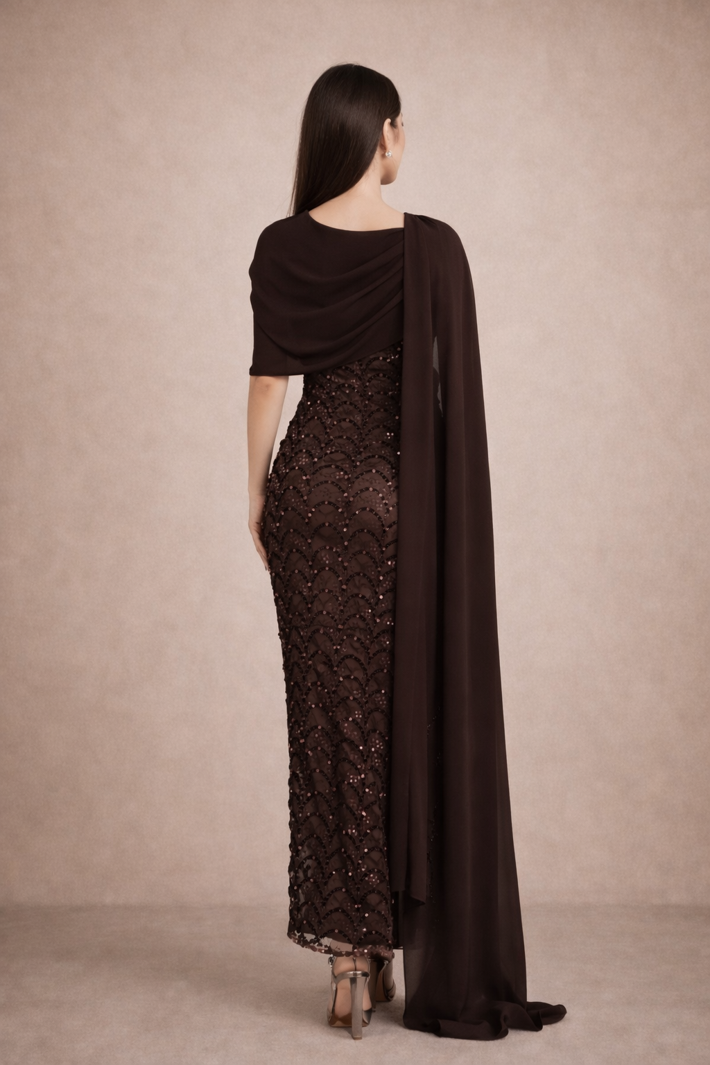 Woman wearing a dark brown lace dress with a matching cape against a beige background