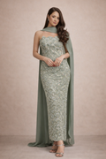 Woman wearing a green lace evening gown with a cape against a beige background