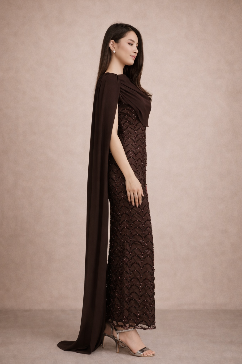 Woman wearing a long brown dress with a cape against a beige background