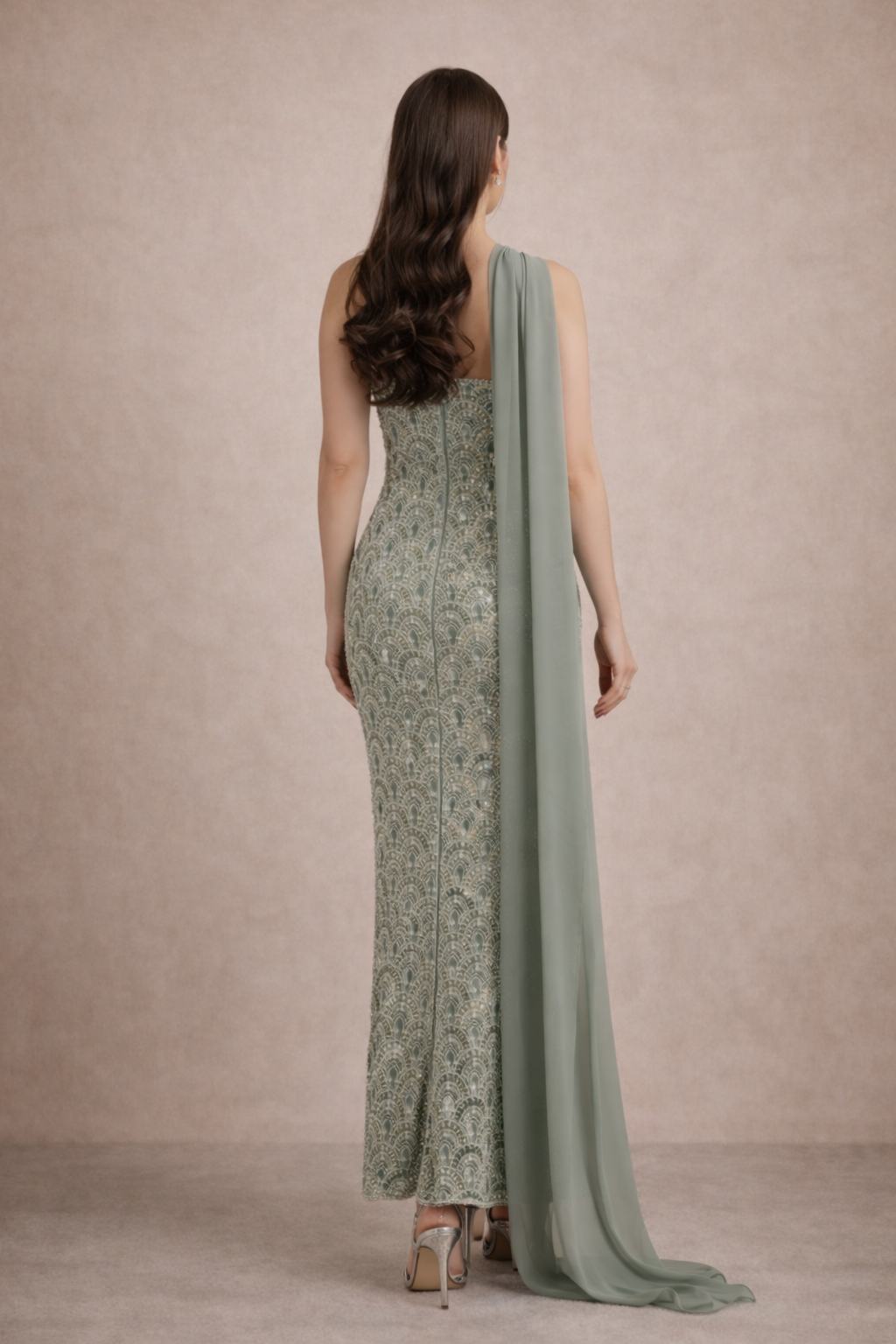 Woman wearing a long, patterned dress with a draped fabric over one shoulder against a beige background.